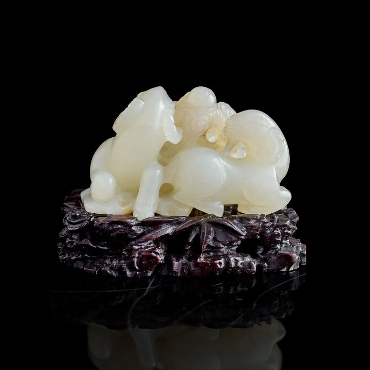 十九世紀早 白玉雕三羊掛墜（附硬木座） A Chinese carved white jade 'three goats' figure, early 19th century